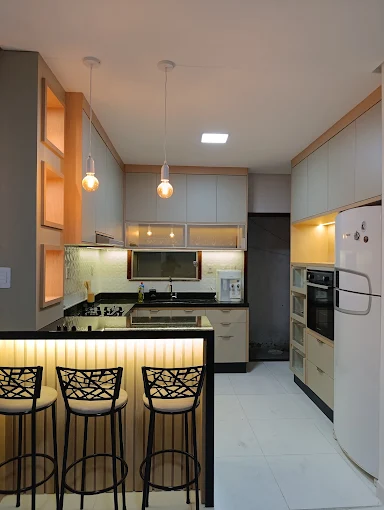 Cozinha planejada com bancada preta, balcão iluminado e nichos amadeirados
