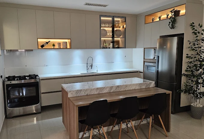 Cozinha planejada com ilha de mármore, mesa de madeira e nichos iluminados